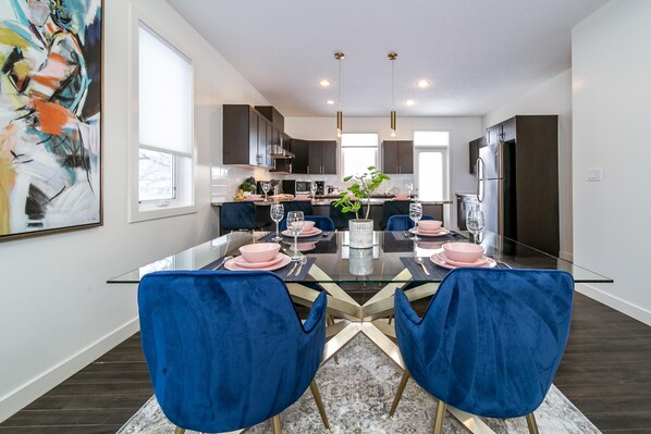 A modern kitchen with dark cabinets, a stainless steel refrigerator, and a dining area with a glass table and blue chairs.