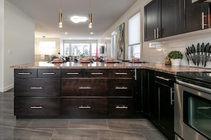 A modern kitchen with dark cabinetry, a granite countertop, and stainless steel appliances.