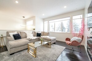 A modern living room with a beige sectional sofa, a glass coffee table, and a pink chair.