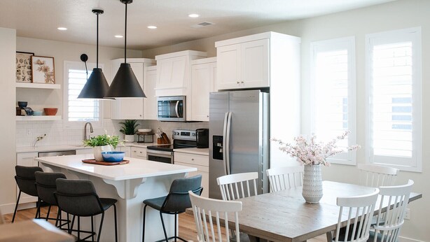 A modern kitchen with white cabinetry, a central island with bar stools, a stainless steel refrigerator, and pendant lighting.