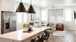 A modern kitchen with a central island, stainless steel appliances, pendant lighting, and a dining area with a sofa and chairs.