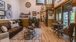 A cozy living room with a brown leather sofa, a coffee table, and a dining area with a wooden table and chairs. There are framed pictures on the walls and a clock. - Hawks Ridge - Eagles Nest home with fireplace, amenities (Banner Elk)