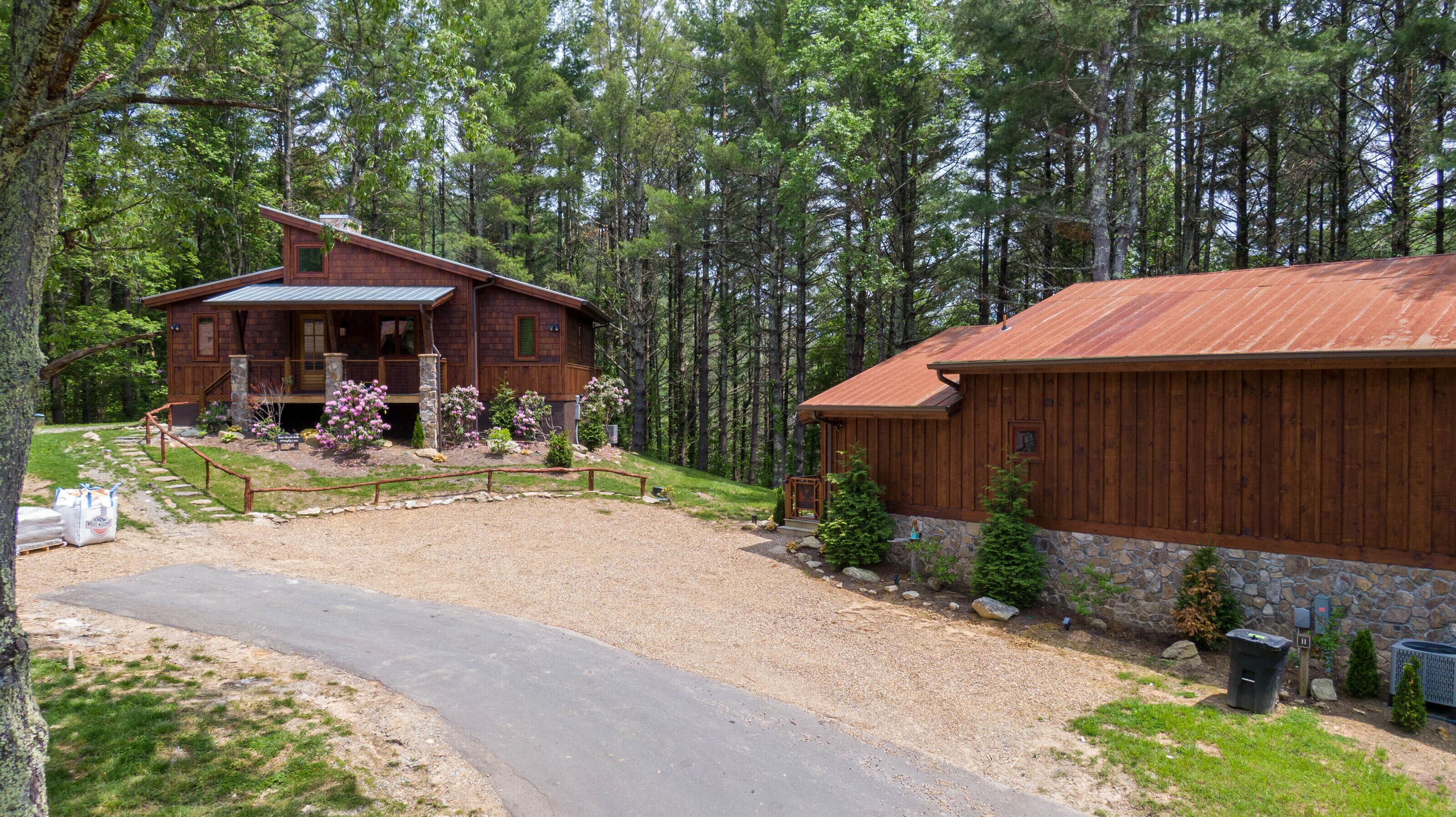 A rustic cabin with a stone foundation and wooden exterior, surrounded by a forested area with a gravel driveway leading to the entrance.