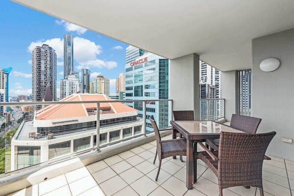 A balcony with a city view, wicker furniture, and a glass railing.