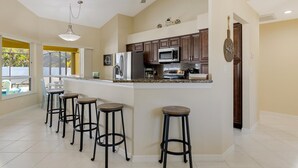 A kitchen with dark wooden cabinets, a stainless steel refrigerator, a microwave, and a gas stove. There are four stools around the island. - Gorgeous heated pool home - Villa Palm Tree - Roelens Vacations (Cape Coral)