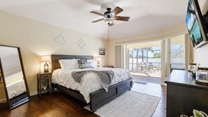 A bedroom with a bed, a ceiling fan, a nightstand with a lamp, and a view of the outdoors. - Gorgeous heated pool home - Villa Palm Tree - Roelens Vacations (Cape Coral)