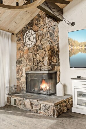 Una chimenea de piedra con fuego, un reloj y un televisor montado en la pared.