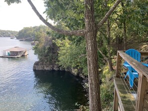 A wooden deck with a blue chair overlooking a calm lake with docked boats.