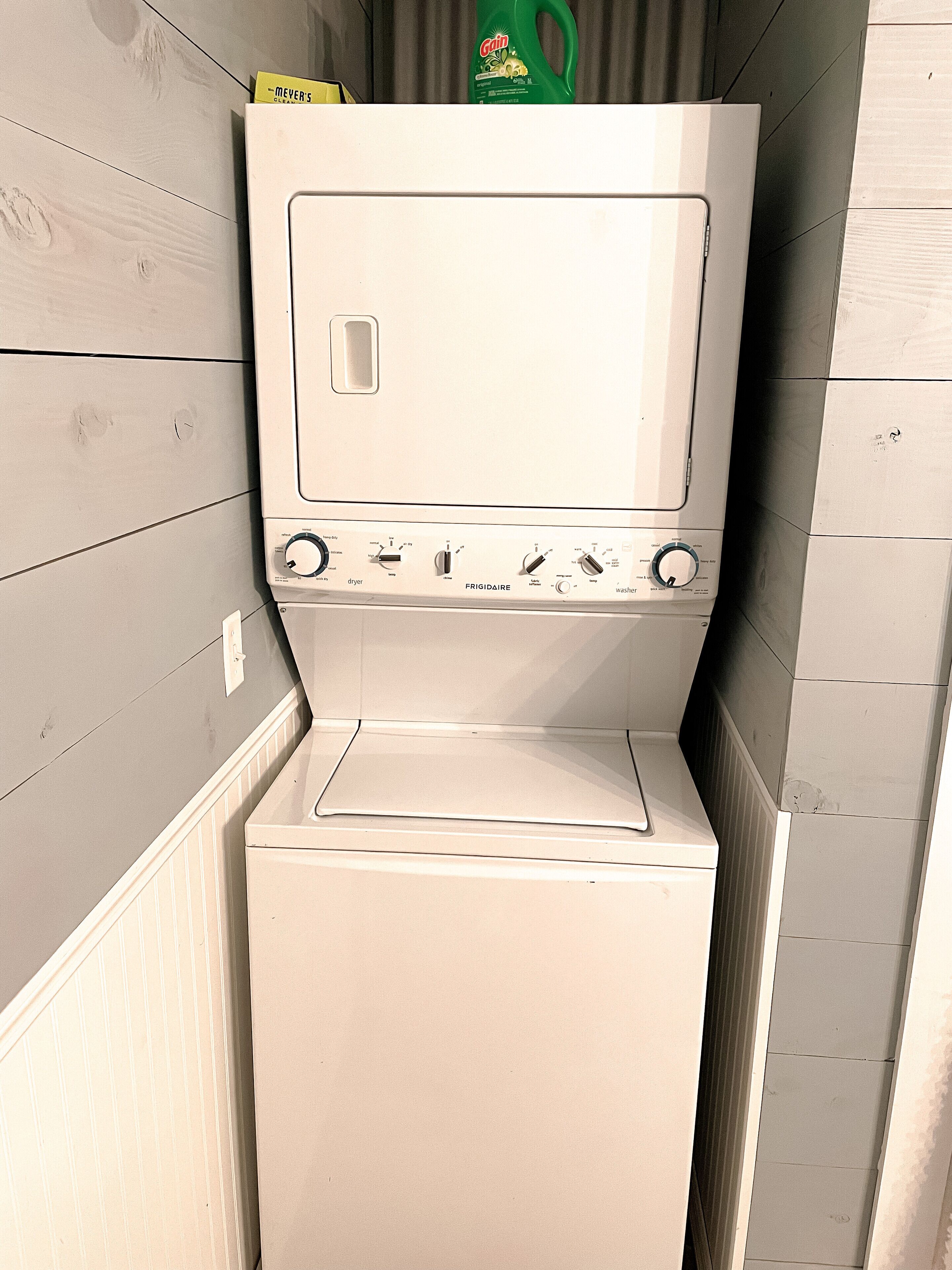 Een compacte wasmachine en droger combinatie met een bedieningspaneel, geplaatst in een hoek met houten lambrisering.