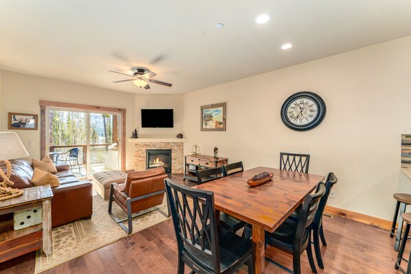 A living room with a fireplace, a dining table with chairs, a sofa, and a TV mounted on the wall.