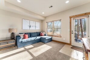 A living room with a sectional sofa, a lamp, a wooden chest, and a door leading outside.