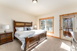 A bedroom with a wooden bed, a nightstand, a dresser, and a door leading to a balcony with a view of trees.