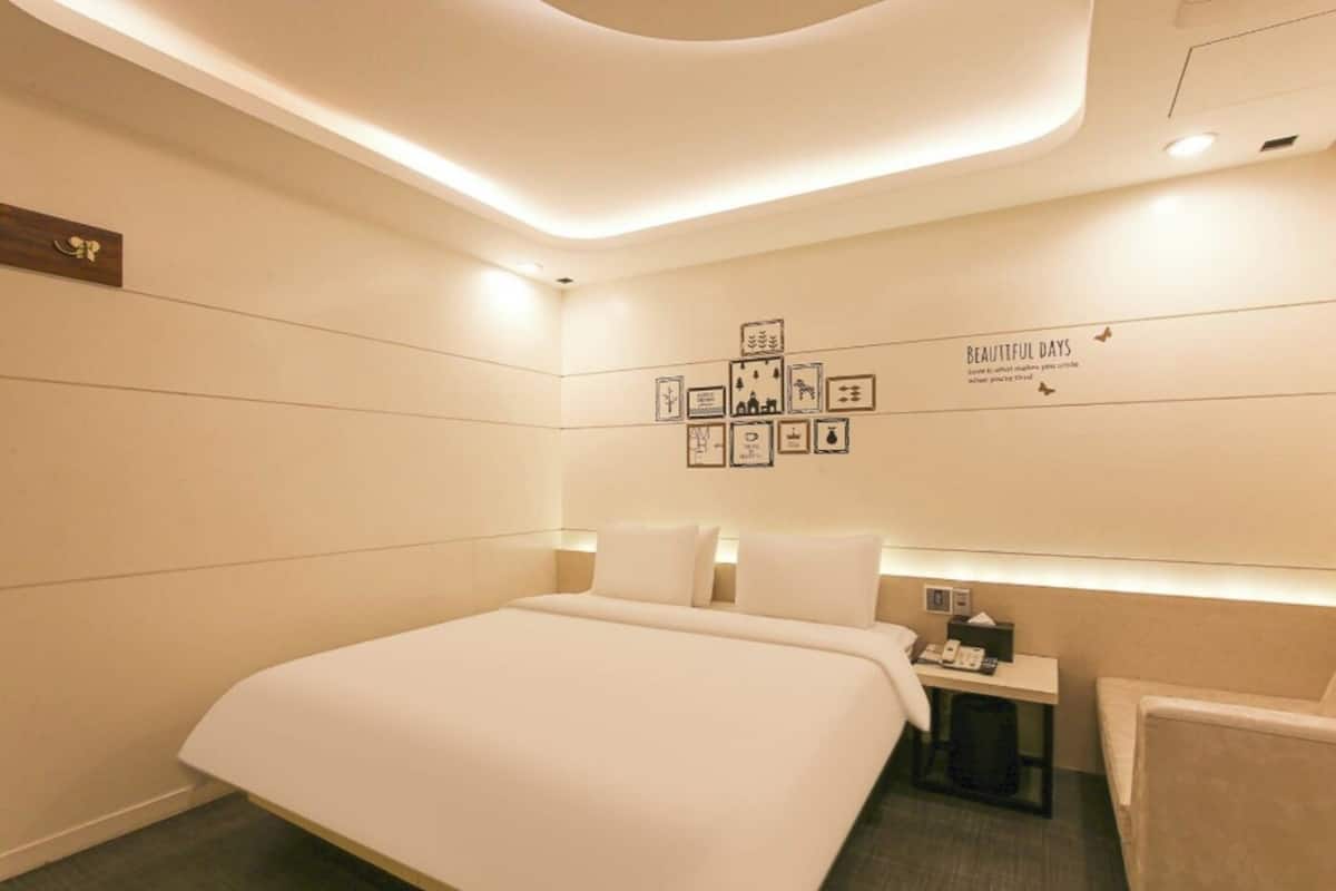 A modern hotel room with a large bed, bedside tables, a nightstand, and a wall with framed pictures and a motivational quote.