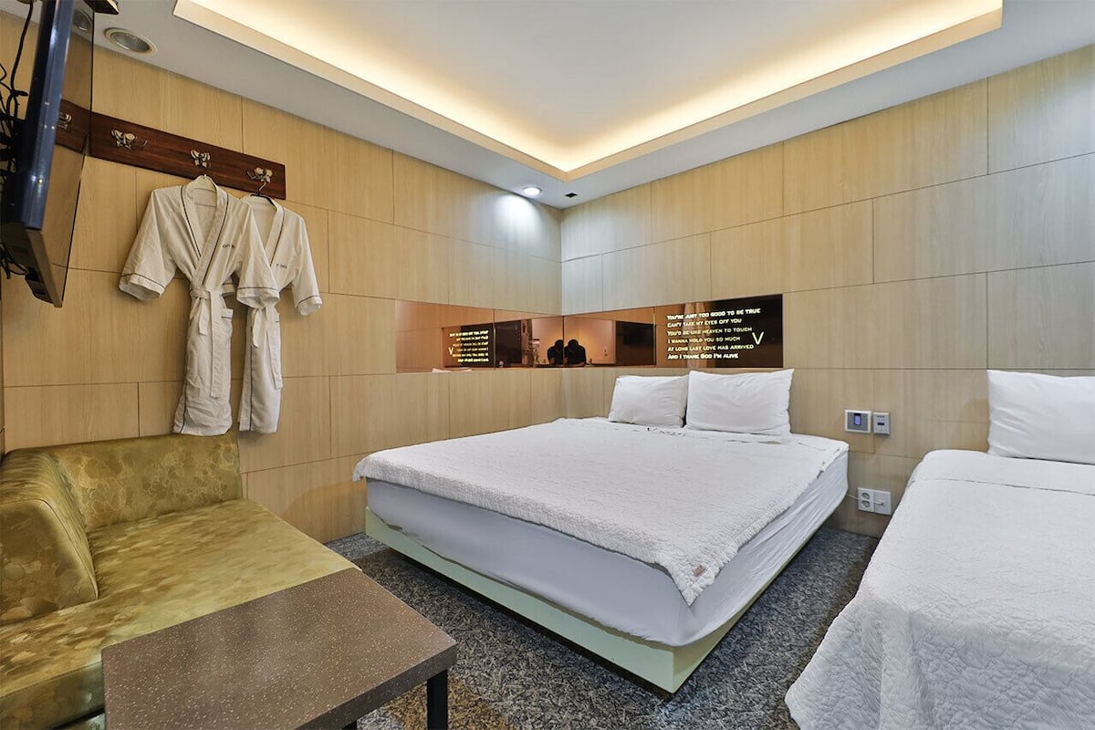 A hotel room with a bed, two bedside tables, a sofa, and a mirror.