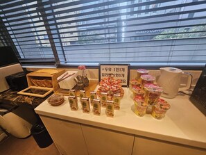 Mostrador de buffet con diversos alimentos y aderezos, una máquina de café y un cartel que anuncia un aniversario de un año.