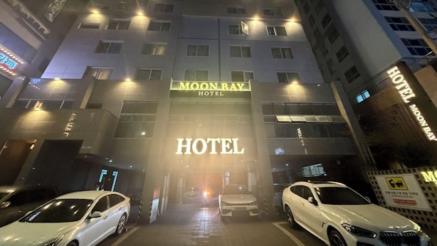 Entrada de hotel con cartel de 'MOON BAY HOTEL', varios pisos y coches aparcados.