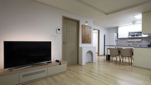 Un apartamento moderno con televisor de pantalla plana, una zona de comedor con sillas, una cocina con armarios y una puerta que da a otra habitación.