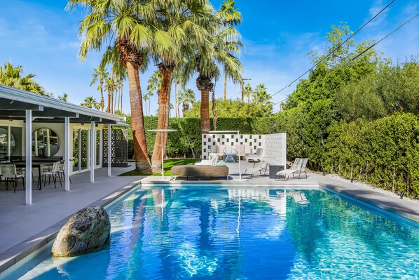 Relax by the rectangular pool surrounded by a deck, lounge chairs, and a seating area with a bench.