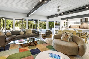 Relax in a spacious living area with comfortable seating and a well-equipped kitchen, offering a view of the surrounding greenery.
