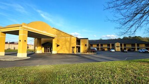 A yellow building with a covered entrance and multiple parking spaces. - Budgetel Inn (Scottsboro)