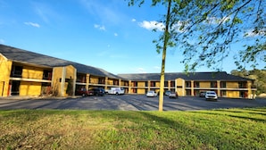 A motel with multiple units, a parking lot, and a grassy area in front. - Budgetel Inn (Scottsboro)