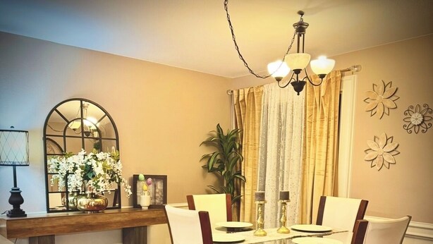 Comedor con mesa de madera, cuatro sillas, candelabro y espejo sobre la mesa.