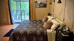 Un dormitorio con una cama, una mesita de noche, una lámpara y un ventanal con cortinas.