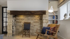 Ein gemütlicher Raum mit einem Kamin aus Stein, einem Holzstuhl mit Kissen und einer Stehlampe.