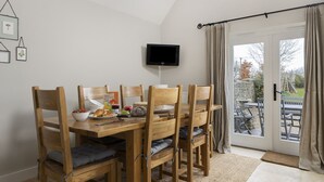 Ein Essbereich mit Holztisch und -stühlen, einem an der Wand montierten Fernseher und Blick ins Freie durch eine Glastür.