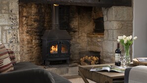 Ein gemütliches Wohnzimmer mit Kamin aus Stein, einer bequemen Couch, einem Couchtisch mit einer Zeitschrift und einer Vase mit Blumen.