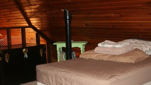 Una camera da letto con soffitto in legno, un letto con copriletto beige, un comodino verde con libri e una valigia nera.