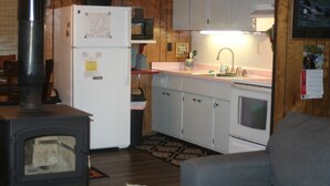 Una cucina compatta con stufa a legna, mobili bianchi, forno a microonde e lavello.