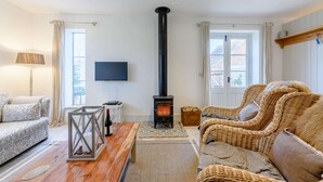 Ein gemütliches Wohnzimmer mit Kamin, bequemen Sitzmöglichkeiten, einem Flachbildfernseher und Blick durch die Fenster.