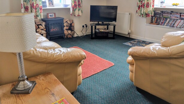 Een gezellige woonkamer met leren banken, een houten salontafel, een open haard, een televisie en een boekenkast vol boeken.