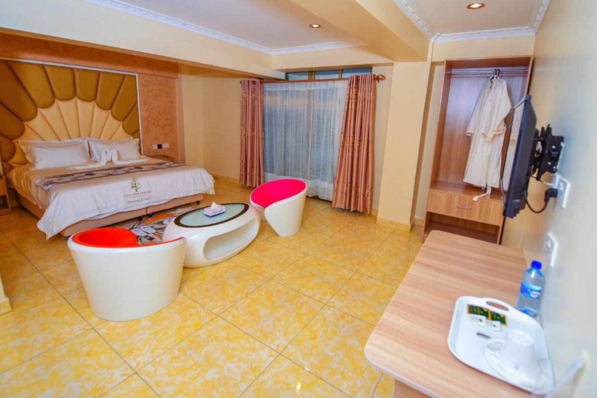 A hotel room with a bed, a small table with a chair, a vanity with a mirror, and a robe hanging on a rack.