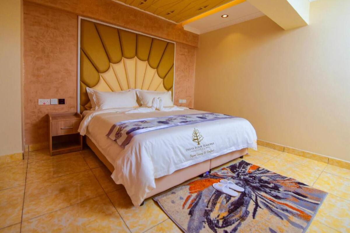 A hotel room with a large bed, a nightstand, a decorative headboard, and a floral rug.