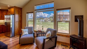 A spacious living room with a large window offering a mountain view, a modern kitchen with wooden cabinets, and a wood-burning stove.