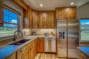 A kitchen with wooden cabinets, stainless steel appliances, granite countertops, and a window with a view of a mountainous landscape.