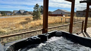 A hot tub with a wooden deck and a view of a residential area with houses and a fence.