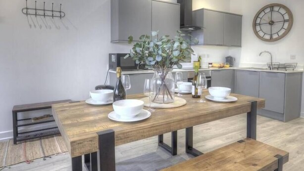 A modern kitchen with a wooden dining table, white bowls, and a vase with green leaves. - The Swell by Guestz (Rhosneigr)