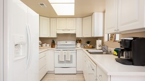 Una cocina moderna con armarios blancos, horno empotrado, cafetera y pileta.