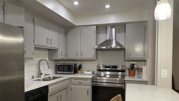 A modern kitchen with stainless steel appliances, white cabinetry, and a wooden dining table. - Beautiful Remodeled West Los Angeles condo - Brentwood adjacent.  (Los Angeles)