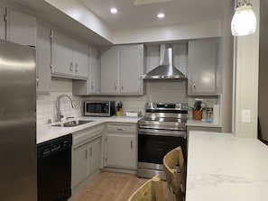 A modern kitchen with stainless steel appliances, white cabinetry, and a wooden dining table.