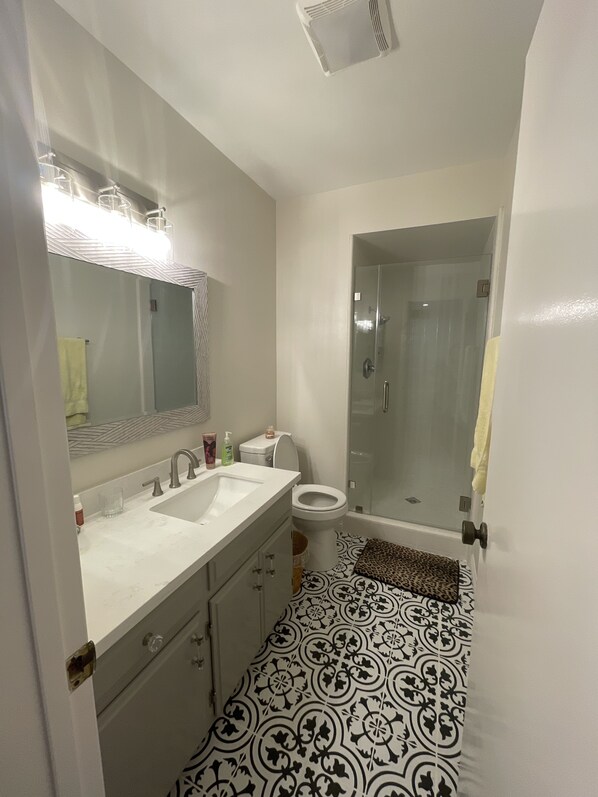 A bathroom with a double sink, a toilet, and a glass shower enclosure.