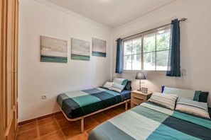 A bedroom with two beds, a window with curtains, and three wall-mounted paintings.