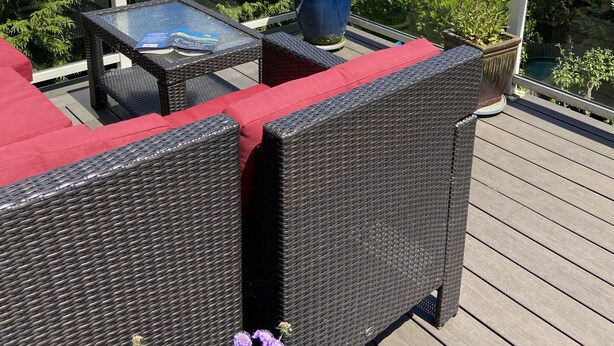 Une terrasse dotée de meubles en osier et d’une table en verre, offrant une vue sur un lac et une zone boisée.