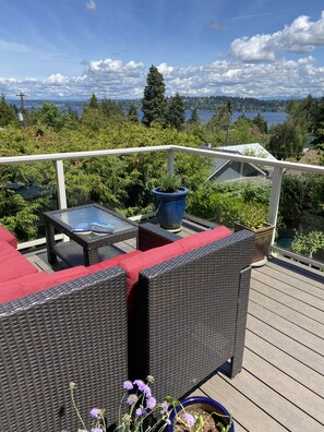 Una terraza con mobiliario de mimbre y una mesa de vidrio, con vista a un lago y una zona boscosa.