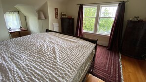 Une chambre avec un grand lit, une fenêtre avec des rideaux, une commode et une lampe.