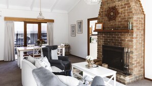 Ein Wohnzimmer mit Kamin aus Backstein, weißen Möbeln und einem Essbereich mit Holztisch und -stühlen.