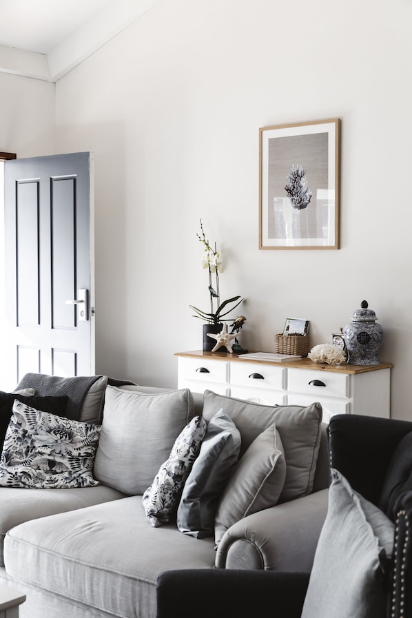 Een moderne woonkamer met een grijze bank, een wit dressoir en een lijstwerk aan de muur.